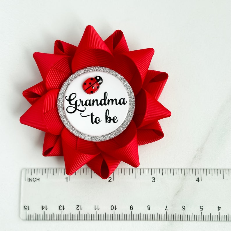 May include: Red and white grandma to be button with a ladybug on it. The button is about 2 inches in diameter.
