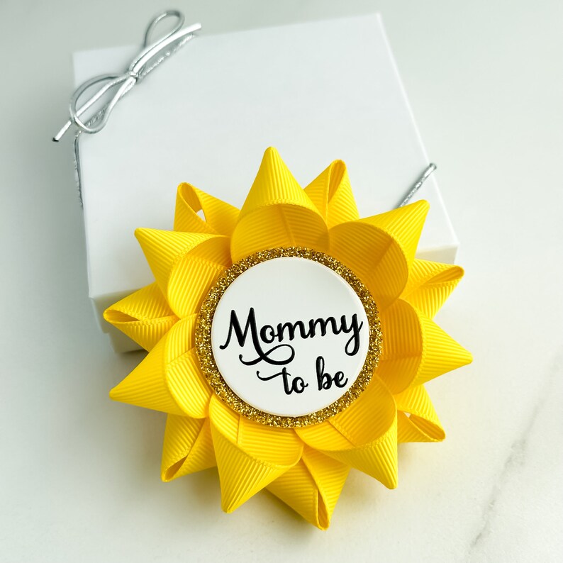 K&ouml;nnte beinhalten: Gelber und goldener "Mama-zu-sein"-Button mit einem wei&szlig;en Kreis und schwarzem Text, der "Mama zu sein" lautet.