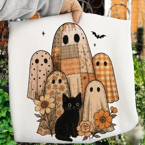 Puede incluir: Bolso tote blanco con una ilustración de Halloween. El diseño incluye cinco fantasmas con disfraces estampados, un gato negro, flores y un murciélago. Los fantasmas tienen varios patrones, incluyendo lunares, florales y cuadros. La paleta de colores es naranja, negro y beige.