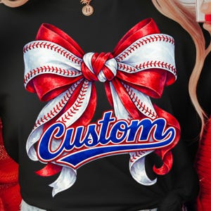 Könnte beinhalten: Schwarzes T-Shirt mit einem Baseball-Themen-Schleifendesign. Die Schleife ist rot und weiß mit Baseball-Nähten, und das Wort "Custom" ist in blauer Schrift mit weißer Umrandung geschrieben.