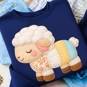 May include: Navy blue sweatshirt with a sheep applique. The sheep has a fluffy white head, pink cheeks, and a floral patterned body. The sheep's body is made of pastel colored stripes. A charming and cozy design.
