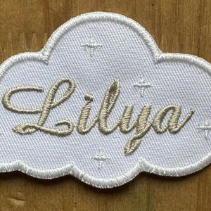 Détail de la broderie haute qualité, fil beige et contour blanc bourdon sur tissu blanc.