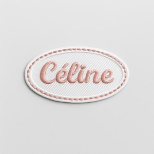 Peut inclure: Un écusson brodé ovale avec le nom "Céline" en cursive rose. Le patch a un fond blanc avec une texture diagonale subtile et une bordure rose en pointillé.
