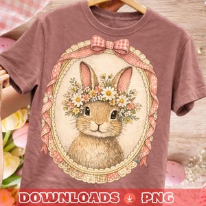 May include: A mauve t-shirt with a watercolour illustration of a bunny wearing a floral crown, set within a decorative oval frame with a pink ribbon and bow. The text "DOWNLOADS PNG" is at the bottom.