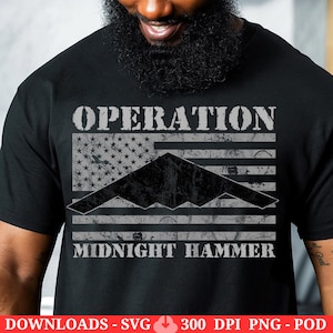 May include: Black t-shirt featuring a distressed American flag design with a stealth bomber silhouette. The text "OPERATION MIDNIGHT HAMMER" is printed above and below the flag graphic in a bold, sans-serif font. The shirt is made of a soft material.