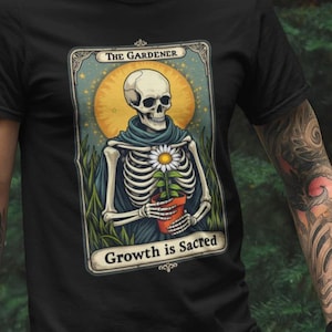 Camiseta con estampado de la carta del Tarot del Jardinero: Esqueleto sosteniendo una margarita. Colores cómodos. El crecimiento es sagrado. Estilo vintage. Camiseta con estética gótica de bruja de jardín.