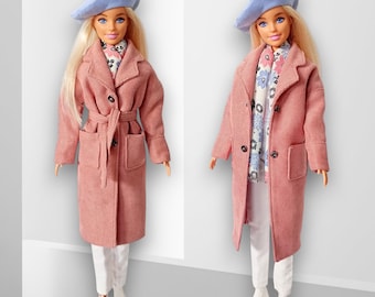 May include: Two dolls are shown, each wearing a light pink coat, white pants, and a light blue beret. One doll has a belt, while the other has a floral scarf. Both dolls have blonde hair and are wearing white boots.