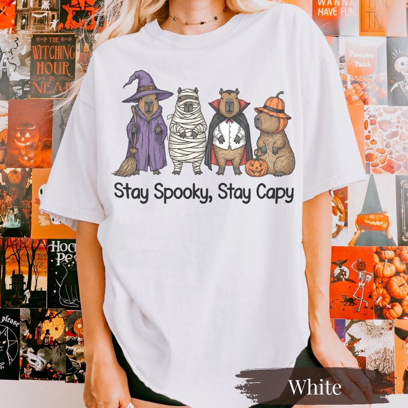 Funny capybara Halloween shirt on classic white Comfort Colors tee. Four capybaras dressed in festive witch, mummy, vampire, and pumpkin outfits make it the ultimate animal lover spooky season shirt. Great gift for capybara fans, zoo animal lovers, and pet parents. Trendy Halloween graphic tee that pairs with flannels and jeans. Light, vintage-washed aesthetic perfect for fall lovers and cozy vibes.