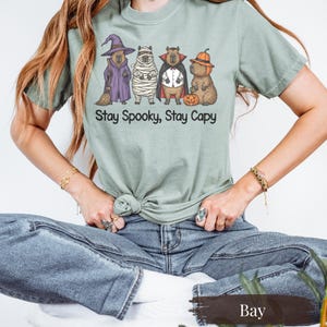 Bay green Comfort Colors capybara Halloween tee with witch, mummy, vampire, and pumpkin capybaras. Vintage-style shirt perfect for animal lovers, spooky vibes, and Halloween humor. Fall shirt idea for pet lovers and fans of capybara memes and cozy oversized fits. Trending capybara Halloween costume graphic on a premium unisex tee. Ideal for trick-or-treating or casual October layering outfit.