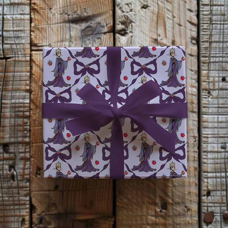 May include: A square gift box wrapped in patterned paper with a repeating design of a queen holding an apple, bows, and apples. The box is tied with a deep purple ribbon and bow, set against a wooden background.