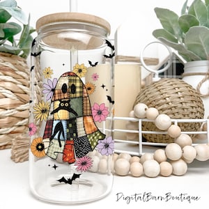Op de afbeelding: Een heldere glazen beker met een houten deksel en rietje. De beker heeft een patchwork spookontwerp met een zwarte kat, bloemen en vleermuizen. De woorden "Digital Barn Boutique" staan onderaan.