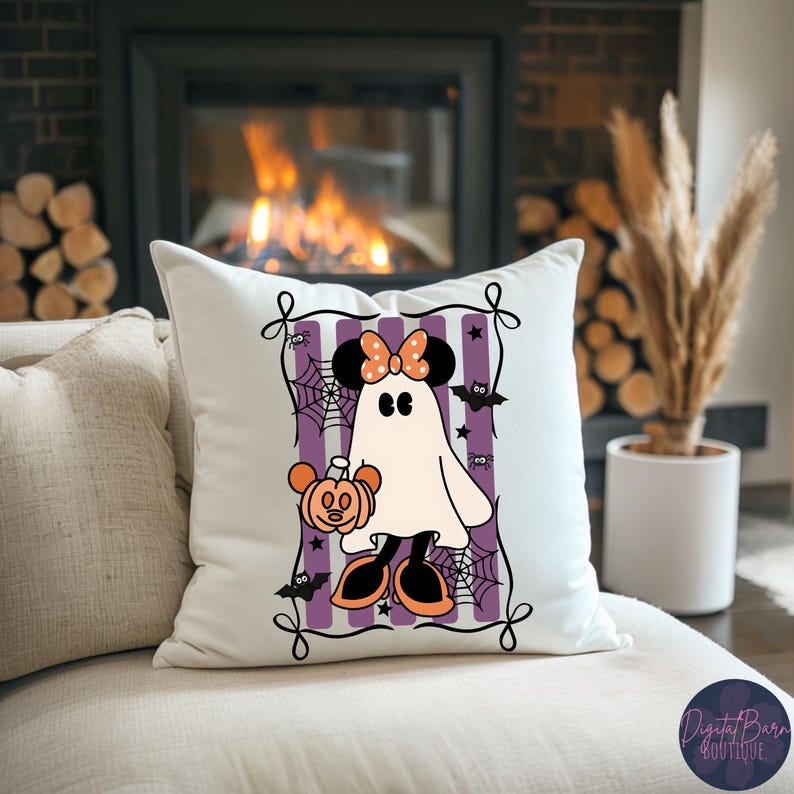 May include: White square pillow featuring a cartoon ghost with a Minnie Mouse bow and holding a pumpkin. The ghost is set against a purple and white striped background, with bats, spiders, and spiderwebs. The pillow is on a white couch.