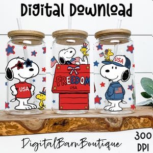 May include: Three glass tumblers with wooden lids and straws. Each tumbler features a different Snoopy design with patriotic themes, including stars, stripes, and the text "USA". The words "Digital Download" and "Digital Barn Boutique" are also visible.