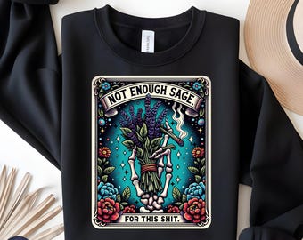Op de afbeelding: Zwarte crewneck sweatshirt met een kleurrijke afbeelding. De afbeelding toont een skelet hand met een bosje lavendel en een brandende sigaret, met de tekst "NOT ENOUGH SAGE" en "FOR THIS SHIT."