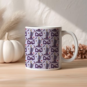 May include: White ceramic mug with a repeating pattern of a cartoon queen holding an apple, purple bows, and red apples on a light purple background. The mug has a white handle and is on a wooden surface.