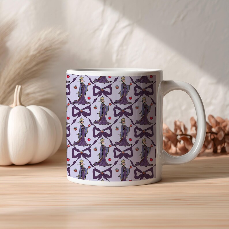 May include: White ceramic mug with a repeating pattern of a cartoon queen holding an apple, purple bows, and red apples on a light purple background. The mug has a white handle and is on a wooden surface.