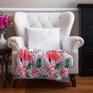 May include: A white armchair with a floral throw. The throw has a pink background with large pink flowers, red centres, and green leaves. A white cushion rests on the chair.