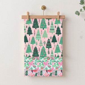 May include: A fabric panel with a repeating pattern of green Christmas trees on a pink backdrop. The lower section shows a floral and bow design in pink and green. The fabric is suspended from a wooden hanger.