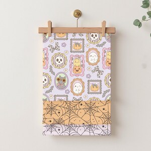 May include: A Halloween-themed fabric panel featuring a repeating pattern of framed skulls, pumpkins, ghosts, and cats in pastel colors. Below, layers of fabric display spiderwebs in orange and white, perfect for seasonal crafts.