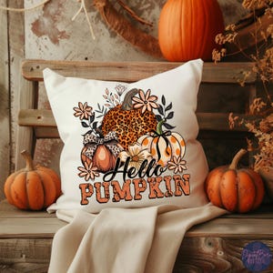 May include: A white decorative pillow with a fall-themed design. The pillow features a leopard-print pumpkin, a pumpkin with polka dots, and the text "Hello Pumpkin" in orange. Two small pumpkins sit on either side of the pillow.