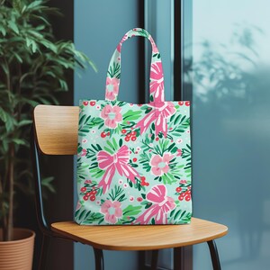 May include: A tote bag with a floral design of pink bows, flowers, and red berries on a pale green backdrop. The bag has matching pink handles. Ideal for carrying shopping or personal belongings, it's made from a durable material.