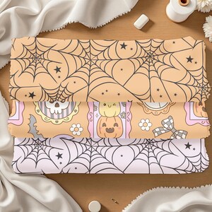 May include: Three stacked fabric pieces with Halloween-themed patterns. The top and bottom fabrics feature black spiderwebs on peach and light pink backgrounds, respectively. The middle fabric has a repeating pattern of pumpkins, skulls, and flowers.