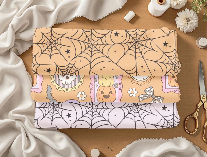 May include: Three stacked fabric pieces with Halloween-themed patterns. The top and bottom fabrics feature black spiderwebs on peach and light pink backgrounds, respectively. The middle fabric has a repeating pattern of pumpkins, skulls, and flowers.