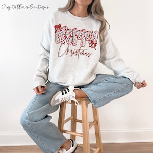 以下が含まれることがあります： フローラルデザインと赤いスクリプトで「Merry Christmas」の文字が入ったライトグレーのスウェットシャツ。スウェットシャツはクルーネックと長袖です。モデルはライトブルーのジーンズと白いスニーカーを着用しています。