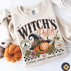 Może przedstawiać: Beżowa bluza z okrągłym dekoltem z nadrukiem graficznym zawierającym tekst Witch's Patch, Spellbound Farm, Locally Grown oraz Potions, Pumpkins, Moonlight Magic. Wzór przedstawia kapelusz czarownicy, dynię, miotłę i gwiazdy.