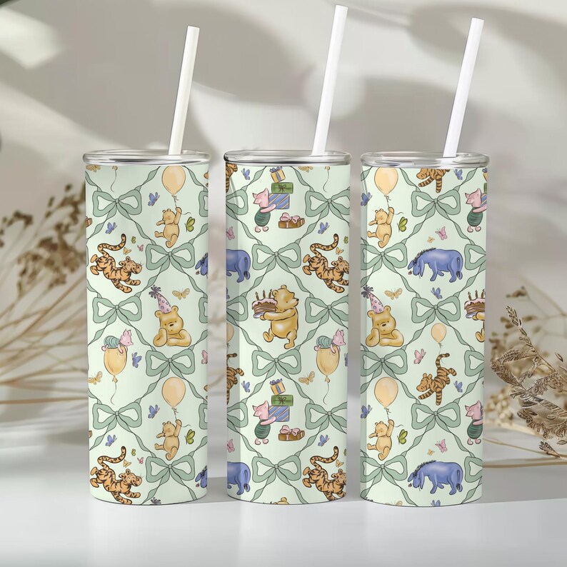 May include: Three insulated tumblers with white straws. The tumblers feature a repeating pattern of Winnie the Pooh characters, balloons, and gifts on a light green background with bows. The design includes Pooh Bear, Piglet, Tigger, and Eeyore.