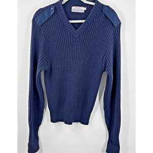May include: Navy blue ribbed knit sweater with a V-neck and shoulder epaulets. The long-sleeved sweater has a label at the neckline and button details on the shoulders. The sweater is hanging on a white hanger.