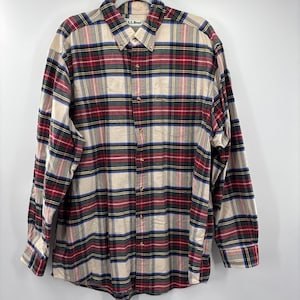 May include: A long-sleeved plaid shirt in beige, red, green, and blue. The shirt has a button-down collar and a chest pocket. The brand name "L.L.Bean" is visible on the collar. The shirt is made of a soft, woven fabric.