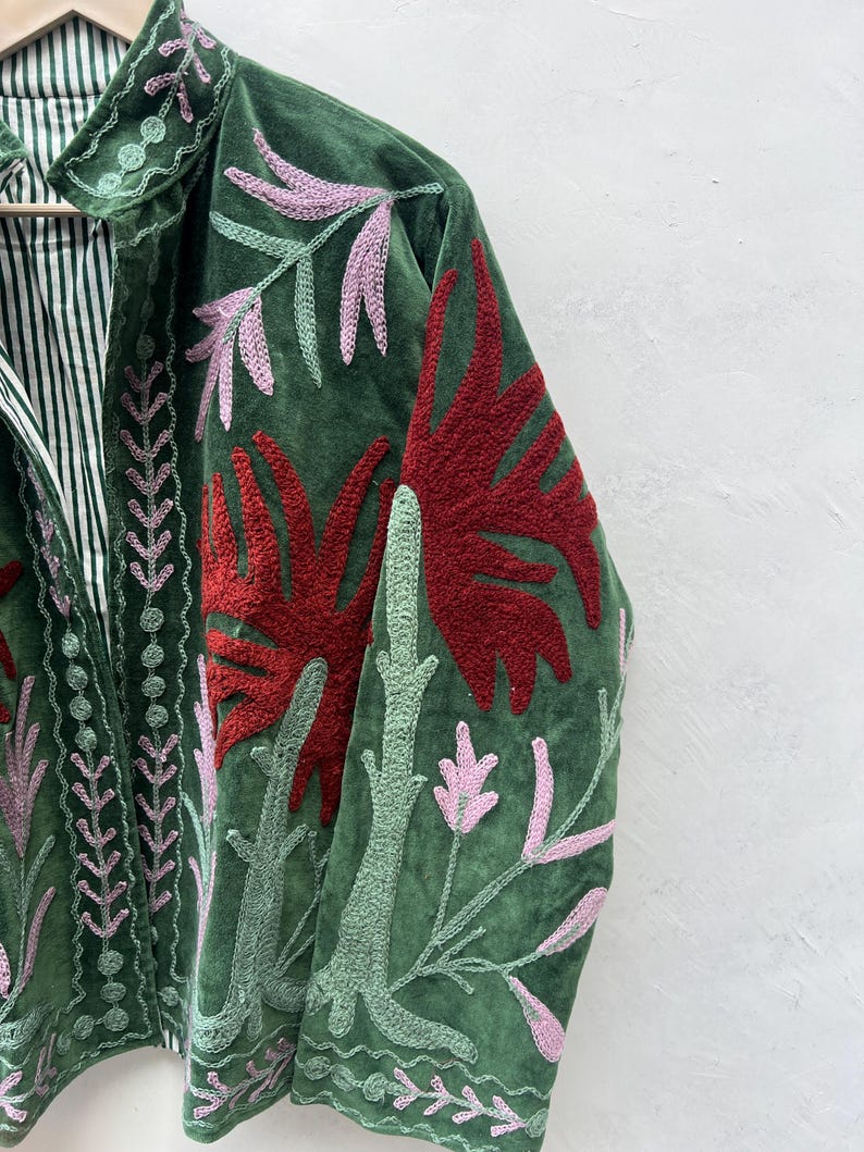 May include: Green velvet jacket with embroidered floral design in red, pink, and green. The jacket features a striped lining and a collar with matching embroidery. A unique piece of apparel.