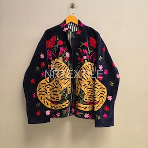 Könnte beinhalten: Eine dunkelblaue Jacke mit lebendiger gelb-schwarzer Tigerstickerei auf den Vorderteilen, akzentuiert durch rosa und rote Blumenmotive. Das Kleidungsstück hat einen Stehkragen und hängt an einem Holzkleiderbügel, wobei der Text NRTEXTILE sichtbar ist.