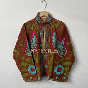 May include: Brown jacket with intricate floral embroidery in teal, red, and green. The jacket features a high collar and a full-length zipper. The text "NRTEXTILE" is visible on the front.