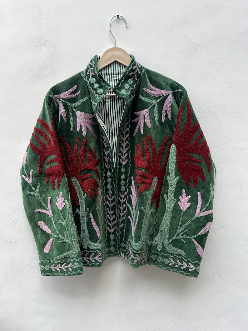 May include: A green velvet jacket with intricate floral embroidery in red and pink. The jacket features a collared neckline and a striped lining. The design includes detailed stitching along the edges and down the front, creating a unique and artistic garment.