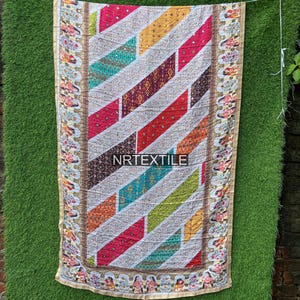 Peut inclure: Un textile coloré avec un motif à rayures diagonales dans diverses couleurs, dont le rouge, l'orange, le jaune, le vert et le bleu. Le textile a une bordure décorative avec des motifs floraux et figuratifs. Le texte "NRTEXTILE" est visible.