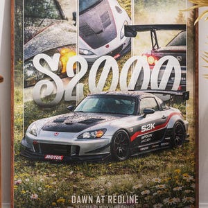 Könnte beinhalten: Gerahmtes Poster mit einem silbernen S2000-Sportwagen mit schwarzen und roten Akzenten, vor dem Hintergrund anderer Autobilder. Das Poster enthält den Text "S2000" und "DAWN AT REDLINE". Das Kunstwerk wird in der Nähe eines Holzstuhls und dekorativer Trockenpflanzen präsentiert.