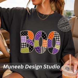 Könnte beinhalten: Ein schwarzes T-Shirt mit dem Wort BOO in einem Patchwork-Design. Die Buchstaben bestehen aus verschiedenen Mustern wie Punkten, Sternen, Karos und Fledermäusen in Orange, Lila, Grün, Schwarz und Weiß. Der Text Muneeb Design Studio ist sichtbar.