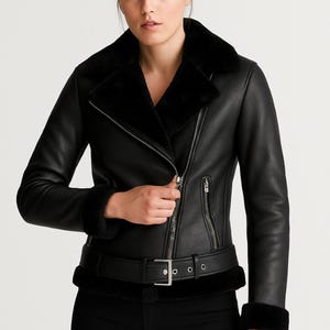 May include: Black faux leather jacket with a faux fur collar and cuffs. The jacket features a silver zipper closure, a belt with a silver buckle, and a tailored fit. A stylish outerwear piece.