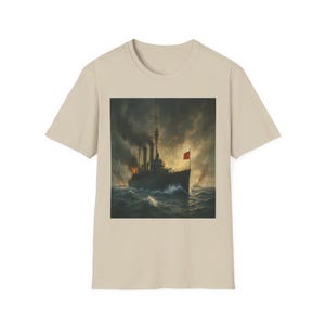 May include: Beige t-shirt with a vintage painting of a battleship at sea. The artwork shows a dark warship with a red flag, amidst stormy waves and billowing smoke. The shirt is a neutral colour.