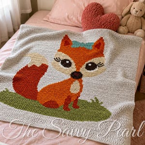 May include: A rectangular crochet blanket featuring a central graphic of a fox with orange fur, a white chest, and a teal bow on its head. The fox sits on a patch of green grass against a light gray background. The text The Savvy Pearl is visible.