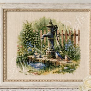 May include: A framed cross-stitch embroidery depicting a vintage metal water pump in a garden setting. The scene features a stone basin with flowing water, lush green foliage, blue and pink flowers, a wooden fence, and four small birds.
