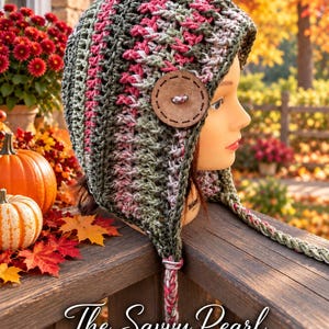 May include: A crocheted earflap hat featuring a variegated yarn pattern in shades of olive green, pink, and grey. The hat is adorned with a large, round, light brown wooden button on the side and includes long, braided yarn ties.