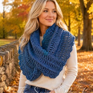 May include: A deep blue crochet cowl scarf featuring an intricate openwork stitch pattern with scalloped edges. The scarf is draped around the neck, showcasing a textured, yarn-based construction with varying shades of blue throughout the design.