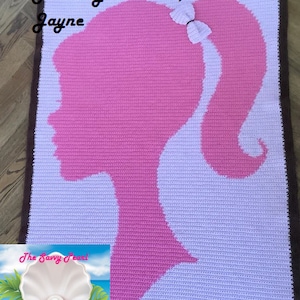 May include: A pink and white crocheted blanket with a silhouette of a woman's head with a bow in her hair. The blanket has a brown border. The text "Made by customer, Jayne" is in the top left corner.