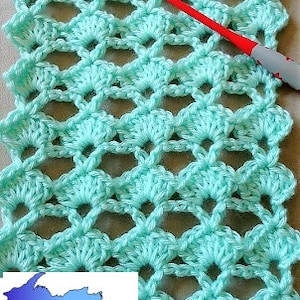 May include: A close-up of a crocheted fabric with a light blue color. The fabric has a repeating pattern of small circles and a crochet hook is visible in the image.