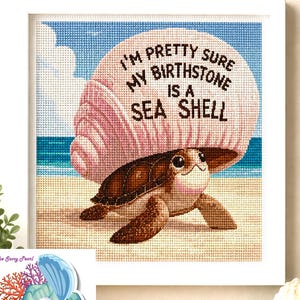 May include: A framed cross-stitch embroidery featuring a brown sea turtle carrying a large pink seashell on its back. The shell displays the black text: I'M PRETTY SURE MY BIRTHSTONE IS A SEA SHELL. The background shows a sandy beach, blue ocean, and sky.