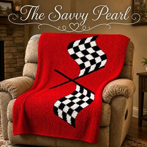 May include: A bright red knitted throw blanket featuring a large, centered graphic of two crossed black and white checkered racing flags. The blanket is draped over a neutral-toned upholstered armchair, showcasing a textured, woven yarn construction.