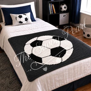 May include: A rectangular crochet blanket featuring a large, centered black and white soccer ball motif. The blanket is crafted with a dark charcoal gray background and a prominent, circular soccer ball design composed of white and black yarn.